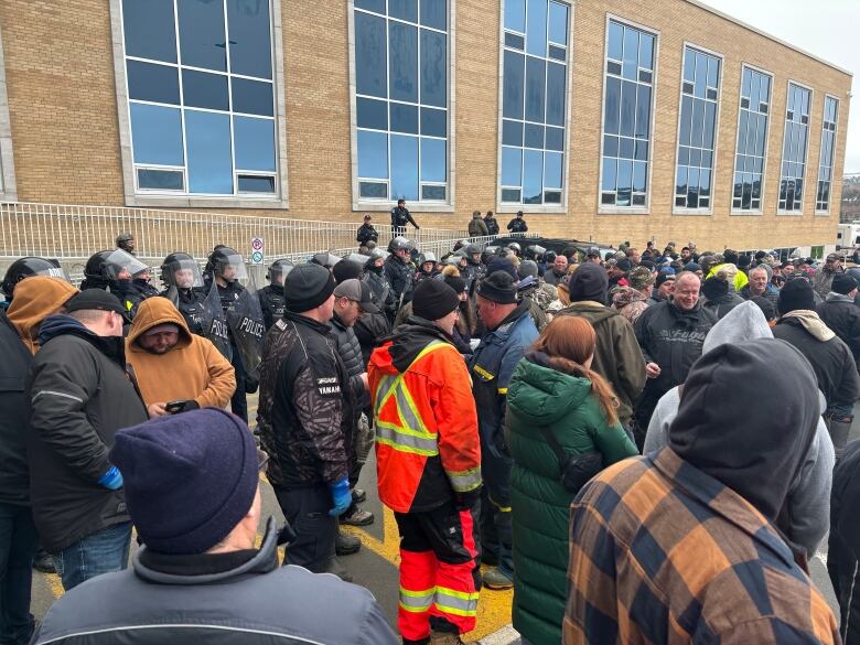 A crowd of people standing in front of police officers wearing riot gear.