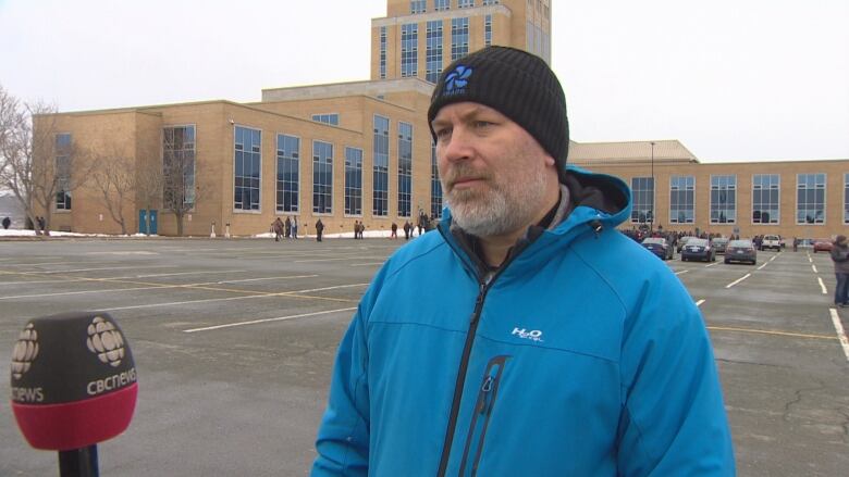 A man wearing a blue coat stands on the parking lot of Confederation Building.