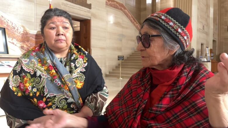 Two women seated in a marble-floored courthouse.