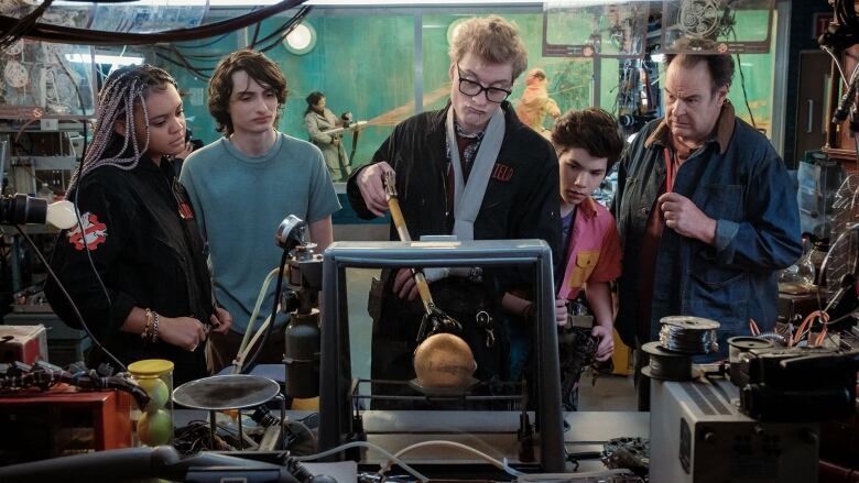 A man holding a mechanical device inspects a golden ball. He is surrounded by four other people.