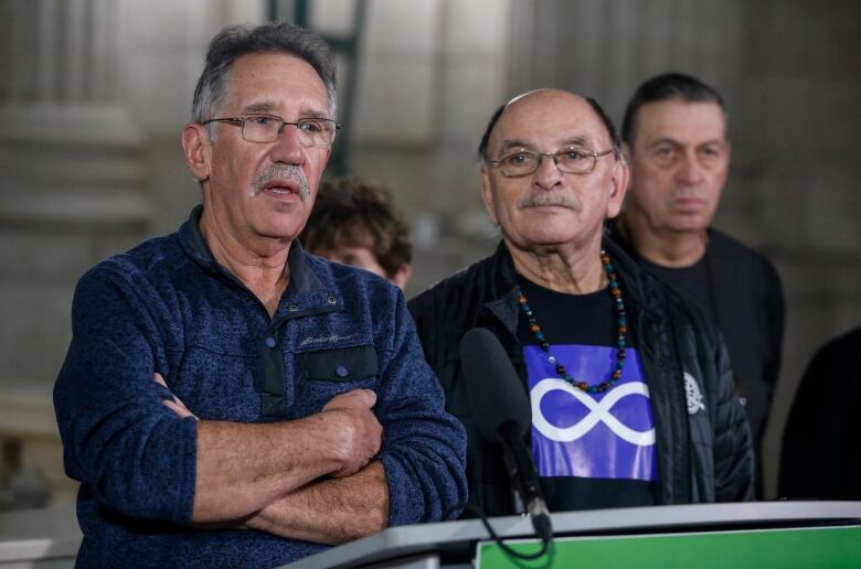 Two men stand at a podium with other people standing in the background.