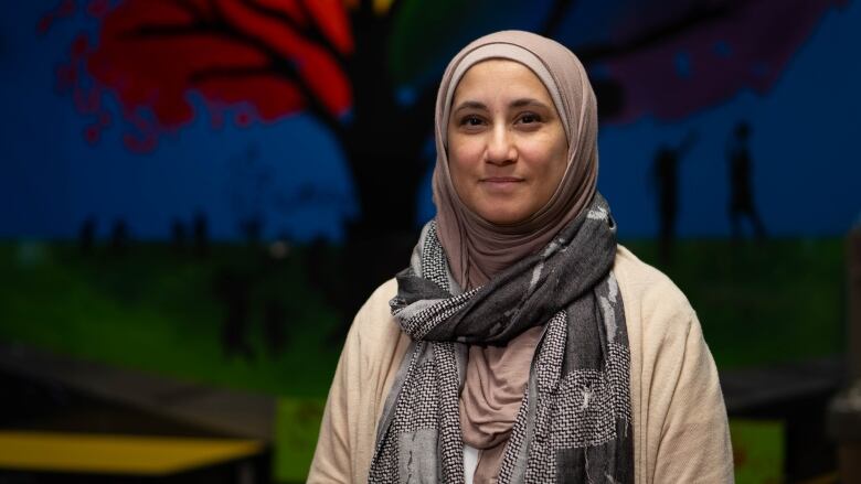 A headshot of a woman wearing a headscarf in front of a colourful mural. 