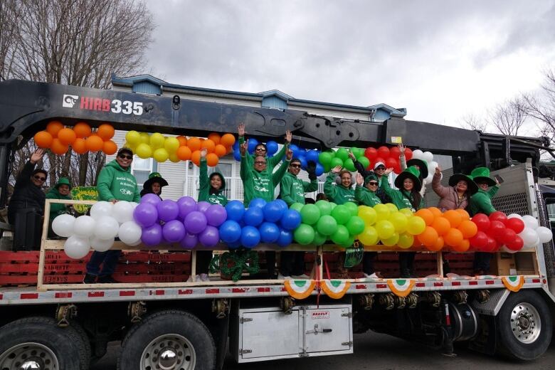 A flatbed truck with waving people and colourful balloons.