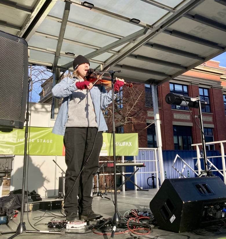 Aleksi Campagne, a white man wearing a blue button-up shirt and black pants, plays the fiddle onstage.