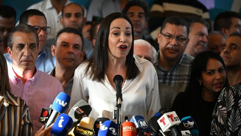 A person speaks into a row of microphones as a group of people stand around them.