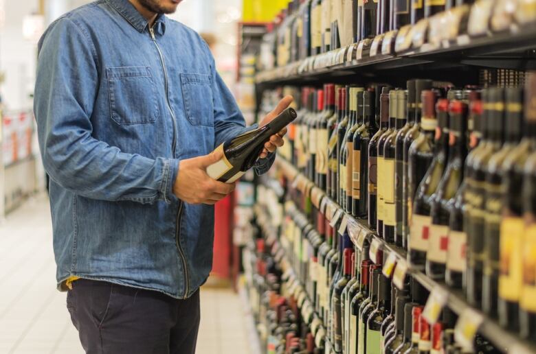 A person holds a bottle of wine at a supermarket aisle.