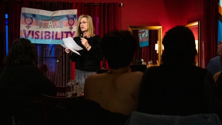 A woman reads a poem on a stage.