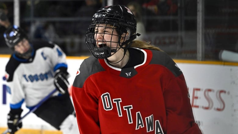 A women's hockey player screams out in celebration while an opponent looks dejected in the background.