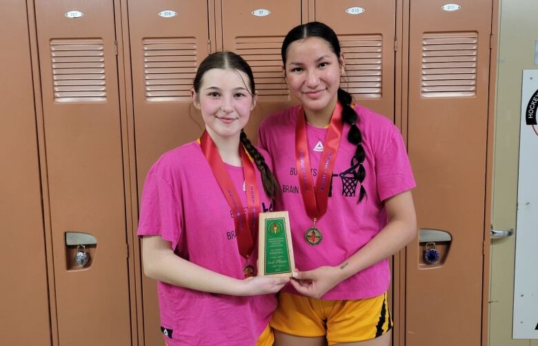 Haylie Cabatoff and Kayla Desjarlais are holding an award and are wearing pink shirts with yellow basketball shorts.