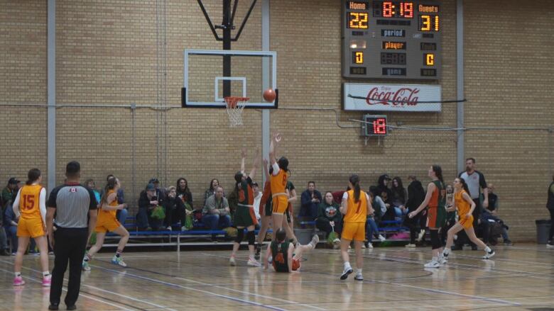 Basketball players are watching a basketball go into the net at an indoor tournament with a crowd in attendance