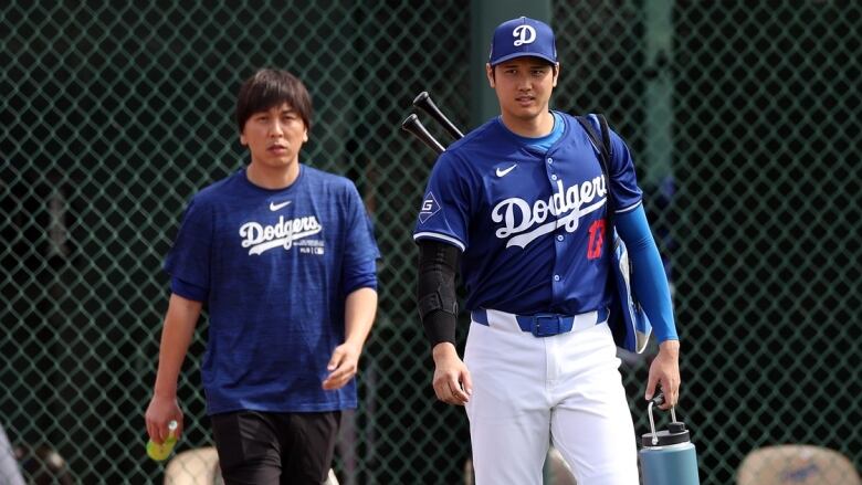 A male baseball player walks onto a field alongside a man wearing street clothes.