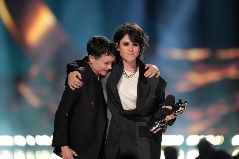 A man leans on the shoulder of a woman holding an award in her hand. 