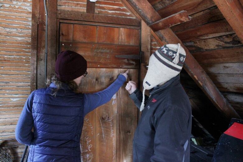 A woman and man point to a wooden door in an attic