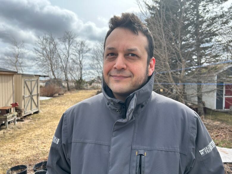 A man with short dark hair in a grey winter jacket standing on a patio in his backyard.