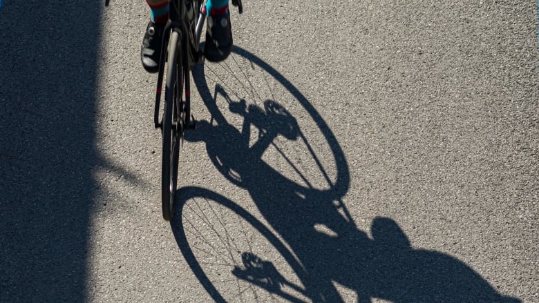 A close of up a bicycles wheels, casting a bicicle-shaped shadow on the gound.