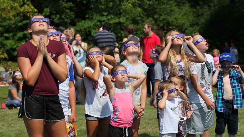 Young people looking skyward, wearing purple protective glasses.