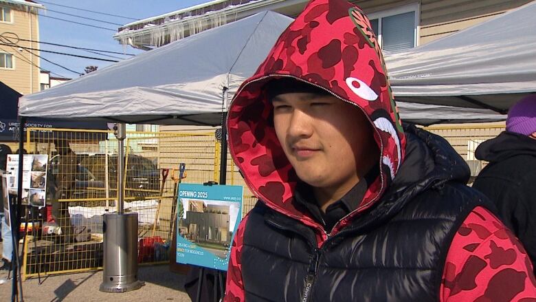 A young man in a red hoodie and black vest. 