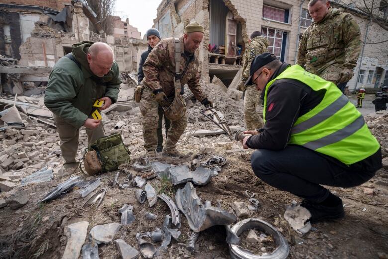 Ukrainian military experts gather remains of a missile next to a destroyed building in the Pecherskyi district