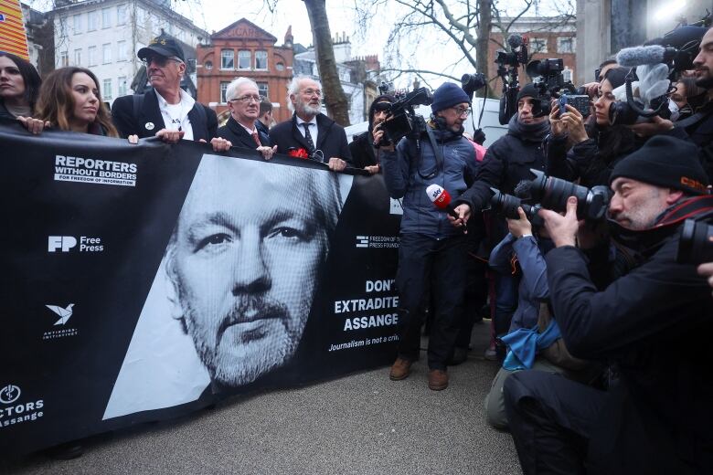 Several people, men and women, unfurl a large banner outside at a demonstration.