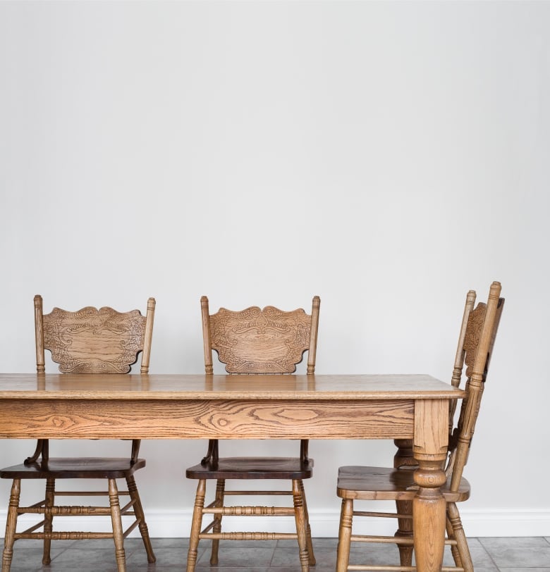 A wooden dining room table with matching chairs sits by a blank wall. 