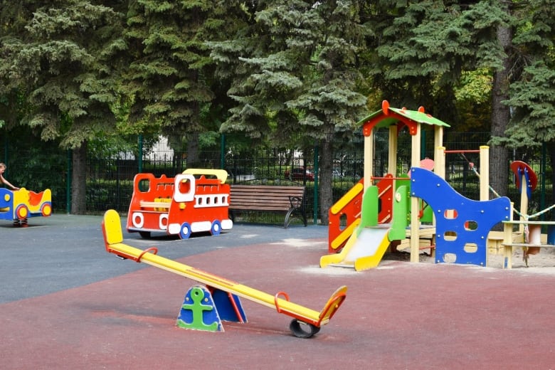 Several pieces of play furniture at a playground, including a teeter-totter, fire engine, slide and playhouse. 