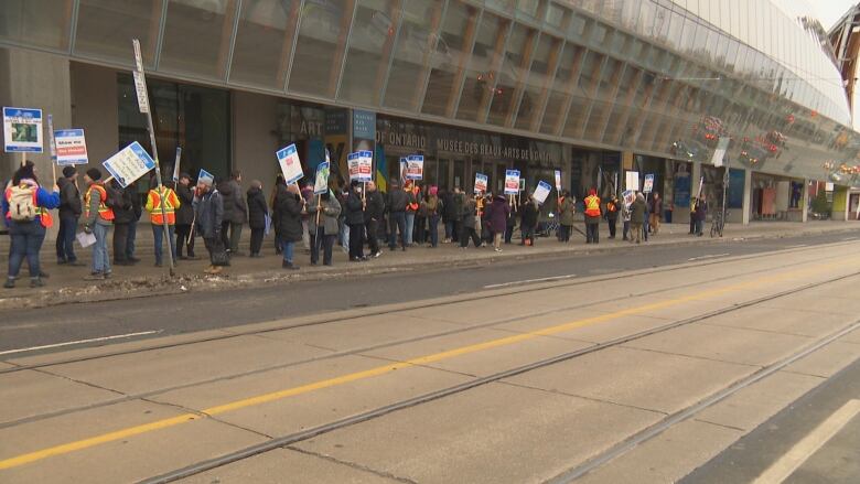 People stand on a sidewalk holding signs.