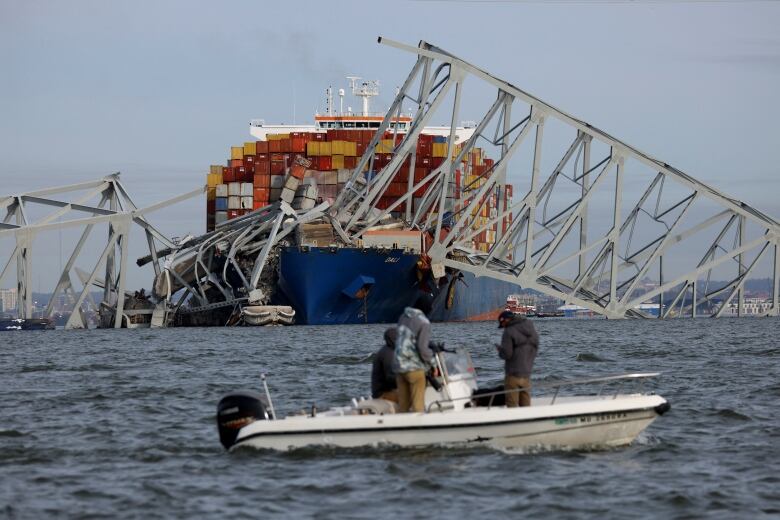 A collapsed bridge lies on top of a massive cargo ship in the ocean.