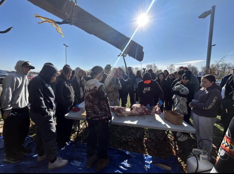 A group of people gather around a table with a deer carcass.