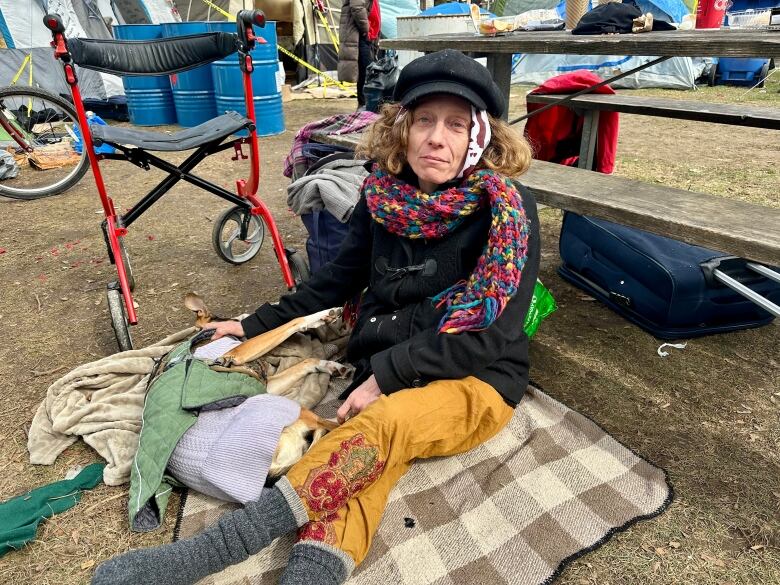 Woman sits on blanket outside with dog