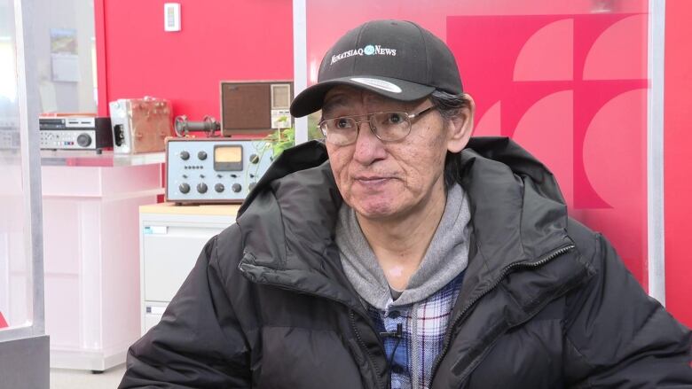 A man wearing glasses and a hat that says Nunatsiaq News looks off to the side of the camera 