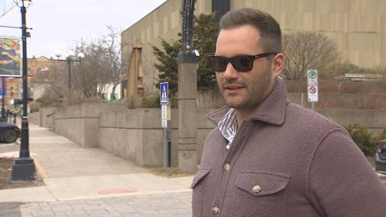 A man in a a light coat and sunglasses answers a question on a downtown Charlottetown street corner.