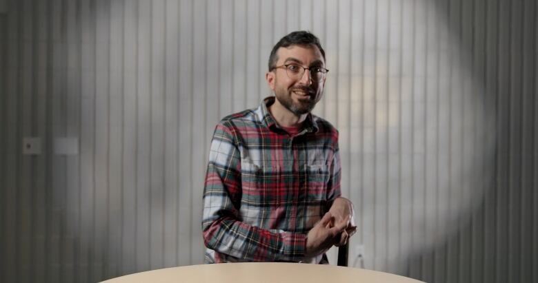 Matthew Burkholder with neutral background. Matthew is wearing a plaid shirt and glasses. He has brown hair. 