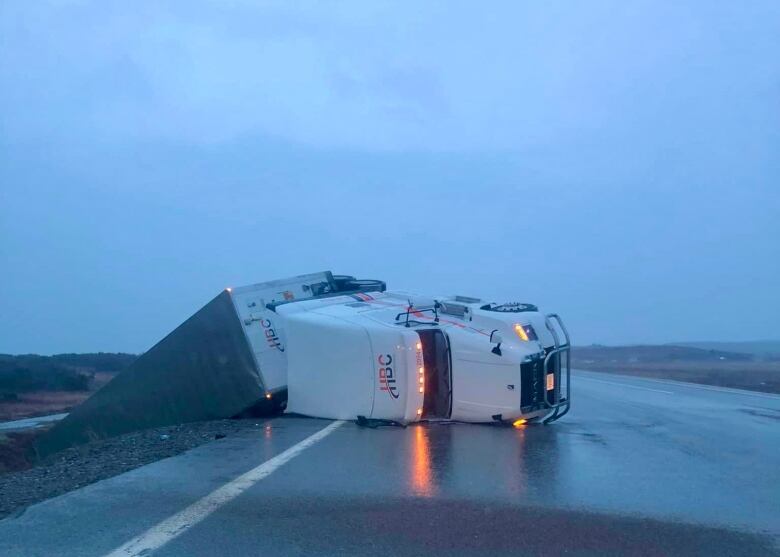 The cab of a tractor trailer and the trailer portion are tipped on their side on the highway.