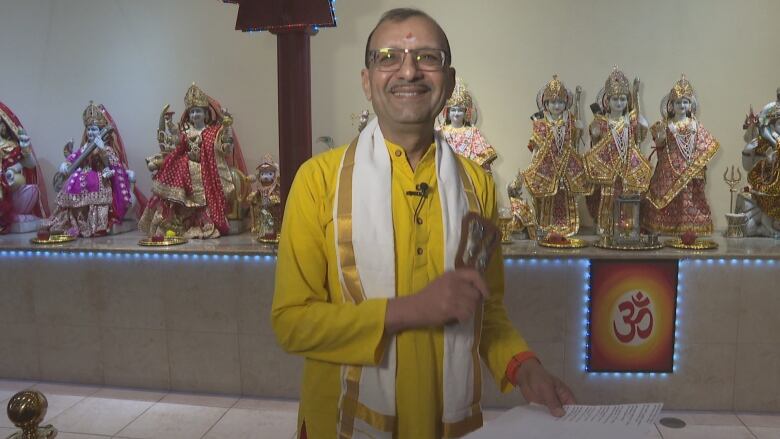 A Hindu priest smiles in front of statues of Hindu religious figures.