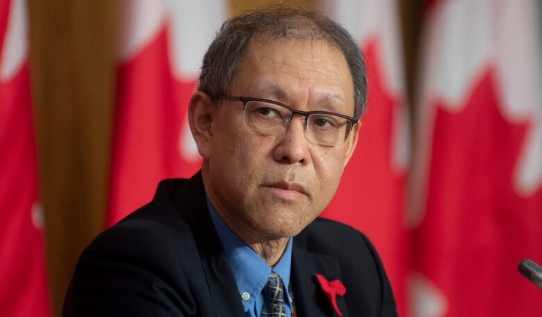 A man looks to his right with Canadian flags in the background.