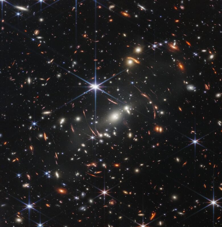 A brilliant white star is surrounded by thousands of galaxies, some that curve.