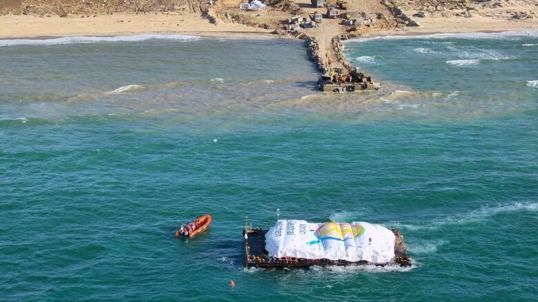 An aerial view shows a barge loaded with food arriving in the water near shore.