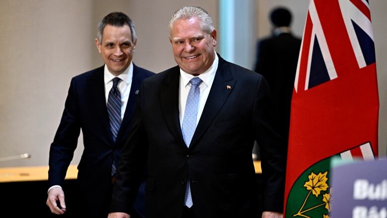 A premier and mayor smile as they walk toward microphones for a news conference.