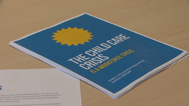 A report sits on a desk. The blue cover reads 'The childcare crisis is a workforce crisis' with a picture of the sun on it.