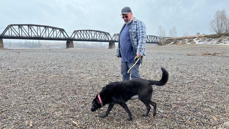 A man walks his dog in a dry riverbed.