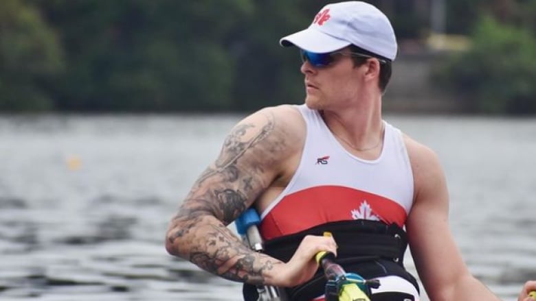 A male Paralympic rower holds onto an oar with his right hand while looking behind him.