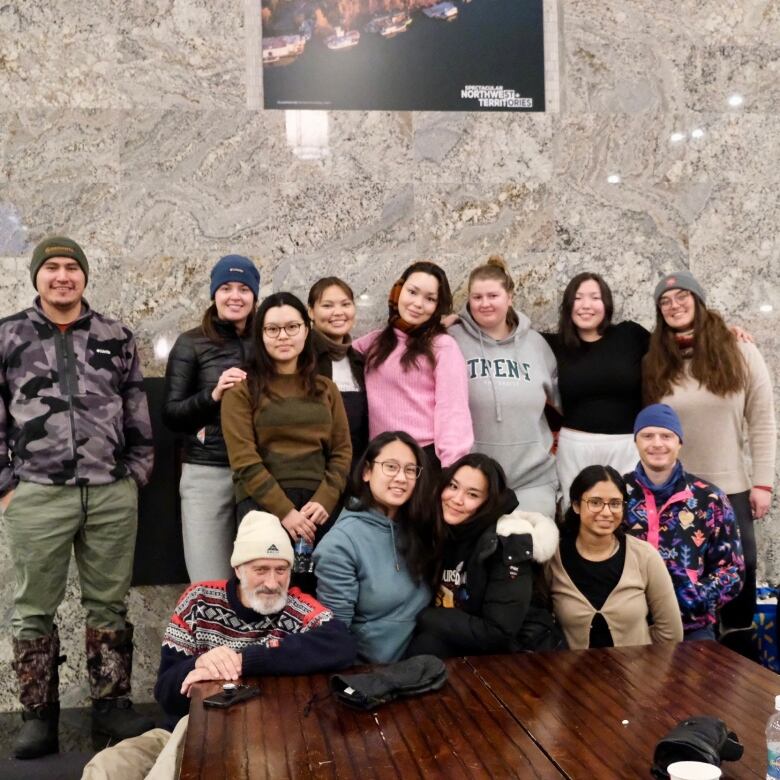 Group of people, 13 altogether, gathered at the end of a table. Posing for a photo.