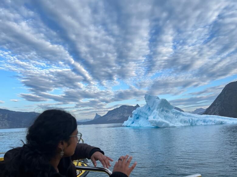 Image of a person at the end or side of a boat, looking out over to a glacier in the water.