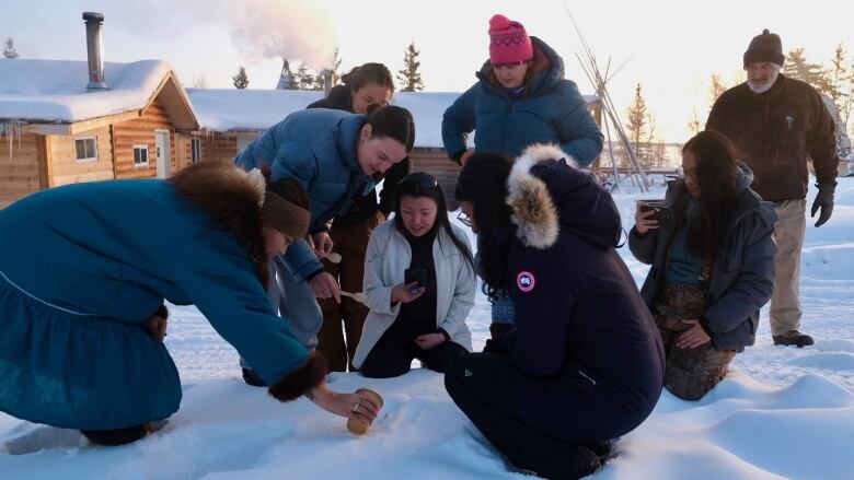 Group of people gathered around a pile of snow holding wooden spoons 