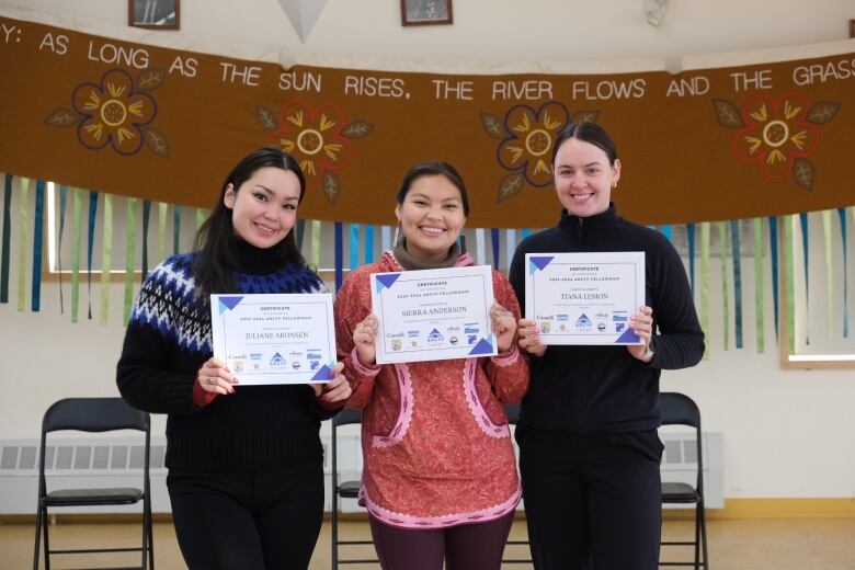 Three people standing and holding out their certificates for the photographer.