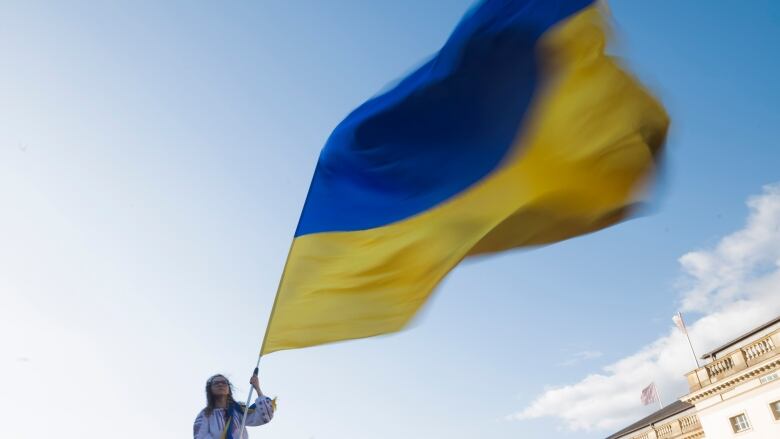 A woman waves a large blue and yellow flag outdoors on a sunny day.