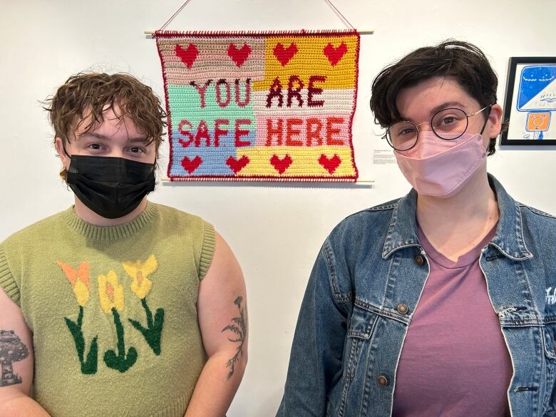 P.E.I. Transgender Network vice-chair Kal Ross, left, and executive director Lucky Fusca with a crocheted artwork behind them reading 