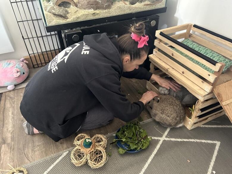 A woman bends over a rabbit crate.