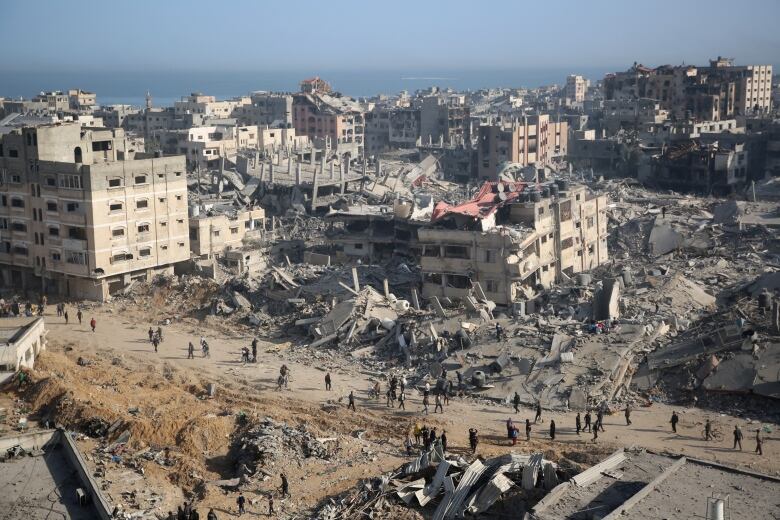 An aerial view shows people walking on a road amid destroyed buildings.