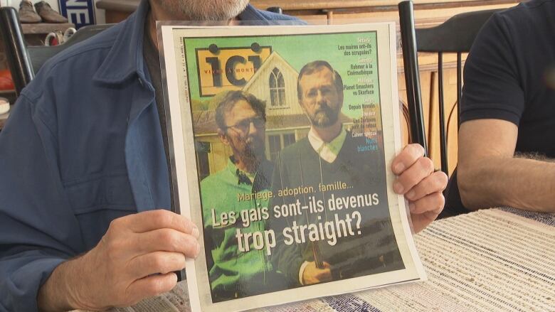 hands holding up a laminated magazine with a photo of a gay couple and the headline 